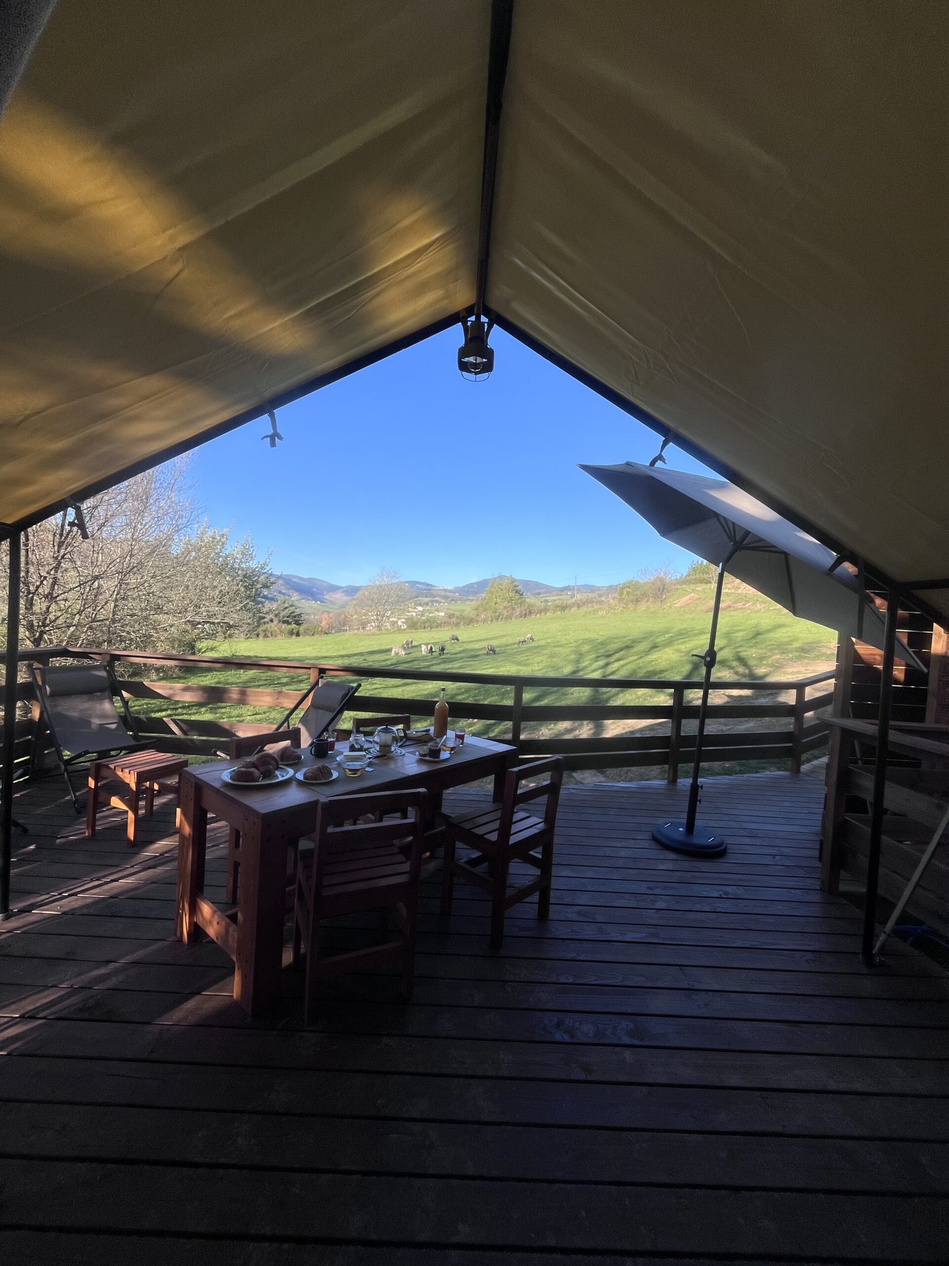 Terrasse en bois de l’Aventura Lodge, table dressée sous la tente safari, ouverte sur la vallée verdoyante