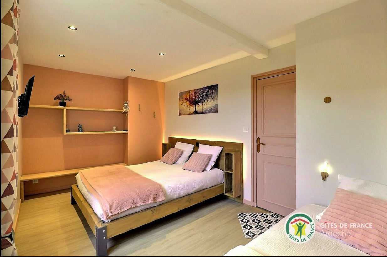 Chambre du gîte avec un lit double, murs ocre et étagères en bois