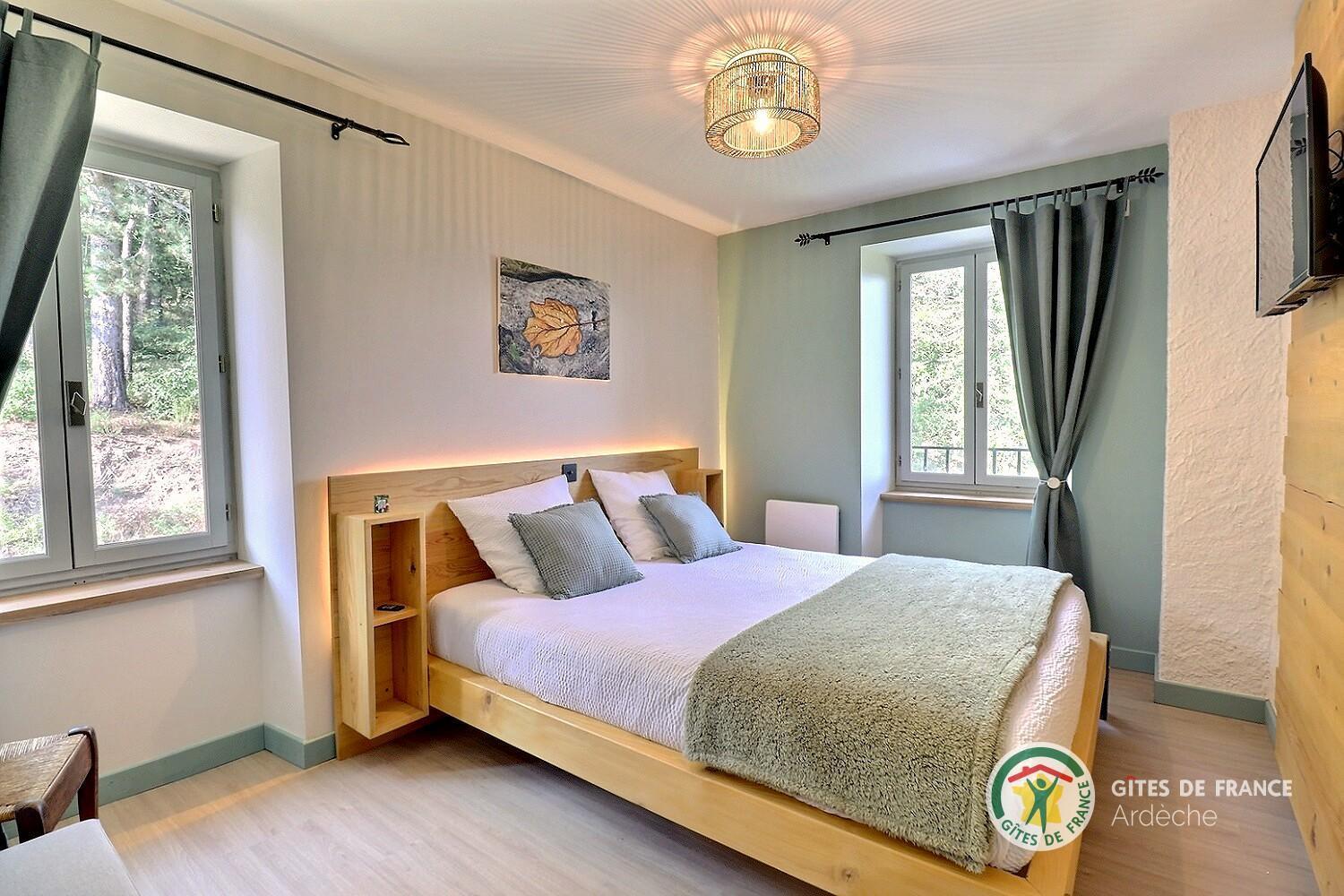 Chambre du gîte avec un lit double face à une fenêtre ouverte sur la forêt