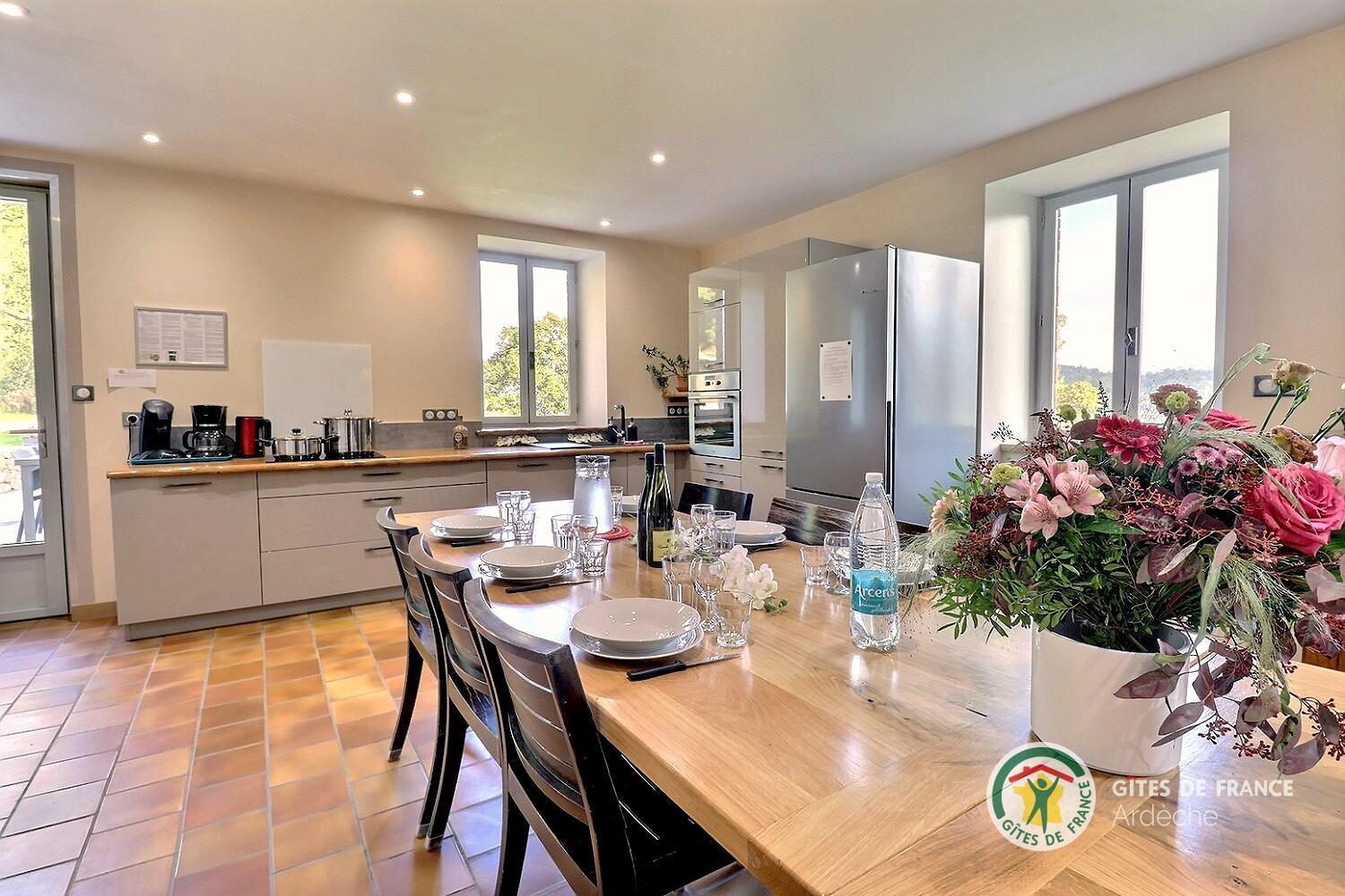 Cuisine équipée du gîte ouverte sur la table dressée, avec un bouquet de fleurs