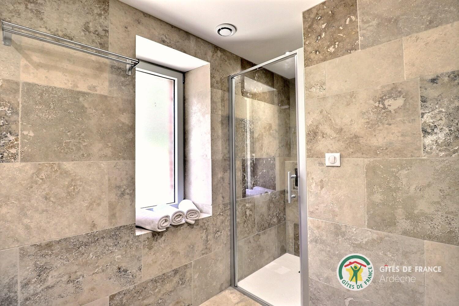 Douche à l’italienne du gîte, paroi vitrée et carrelage travertin