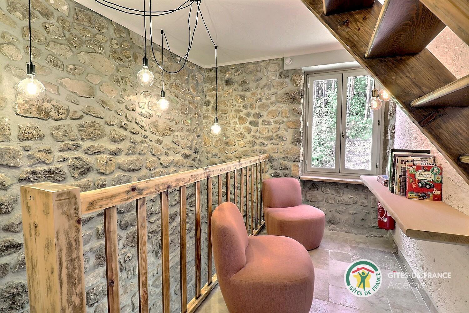 Mezzanine du gîte avec fauteuils, bibliothèque et mur de pierre apparente
