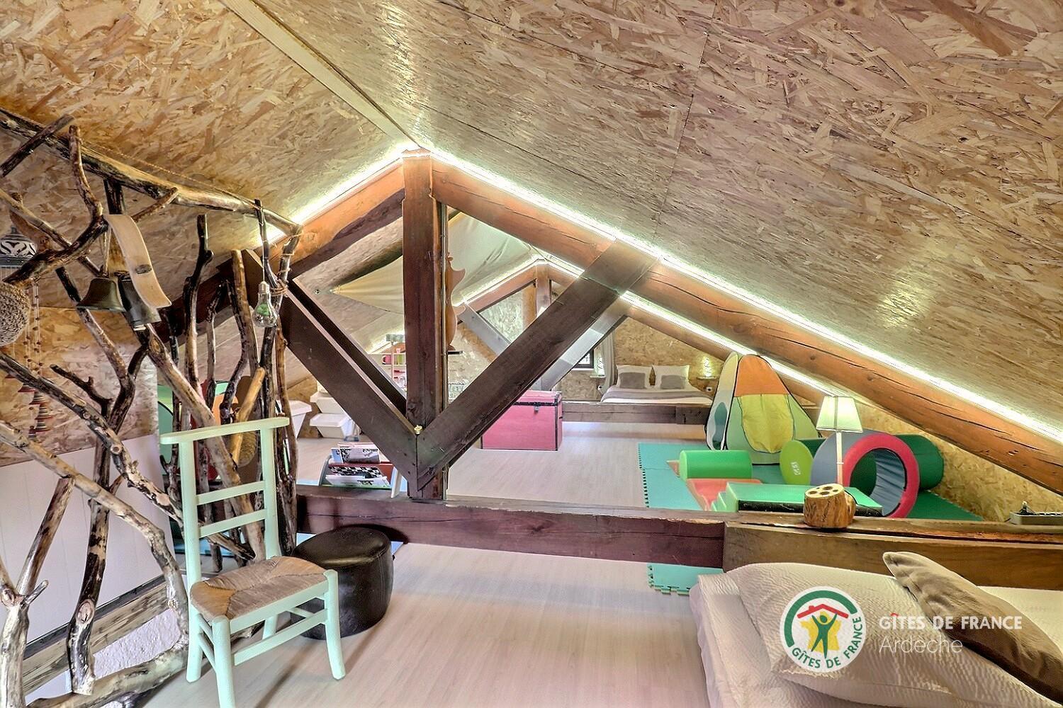 Salle de jeux aménagée dans les combles du gîte, charpente apparente et jouets pour enfants