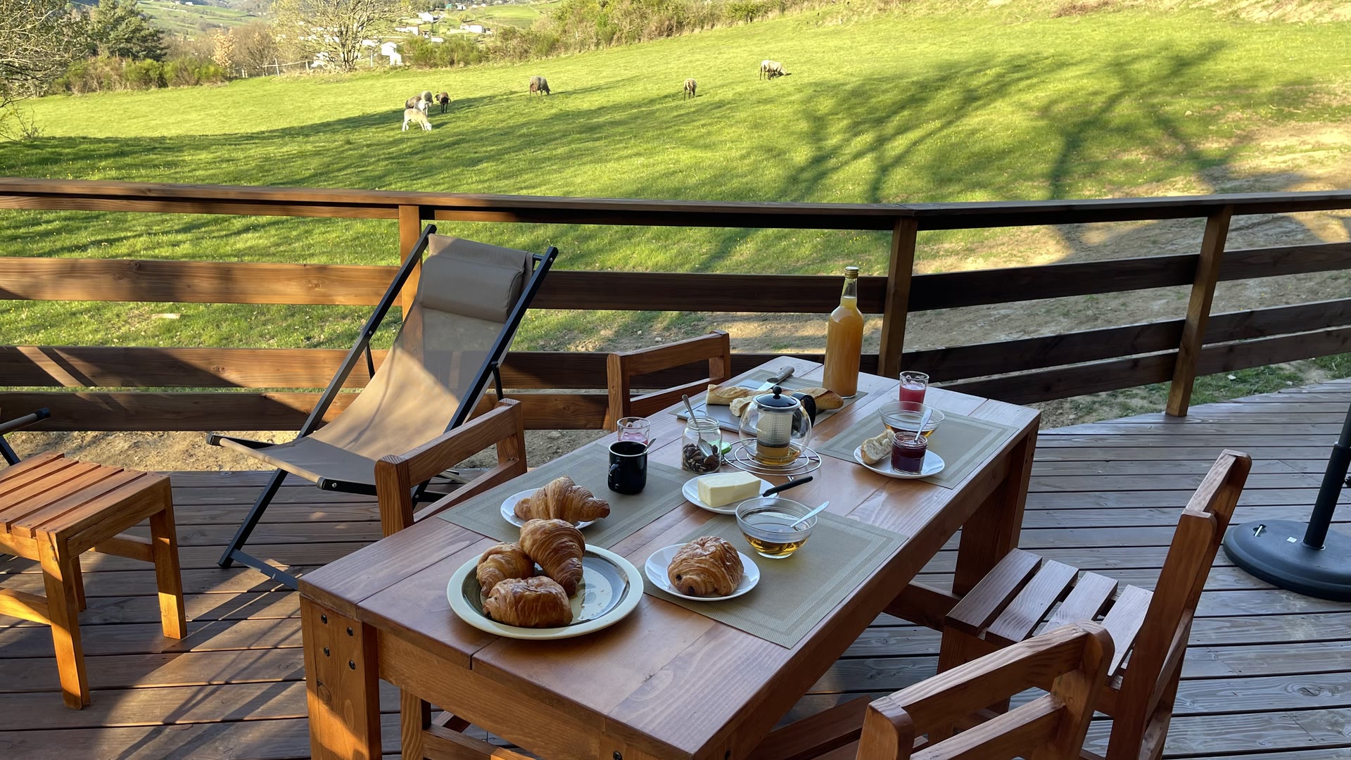 Petit-déjeuner servi sur la terrasse en bois de la tente safari, le pré et les moutons en arrière-plan