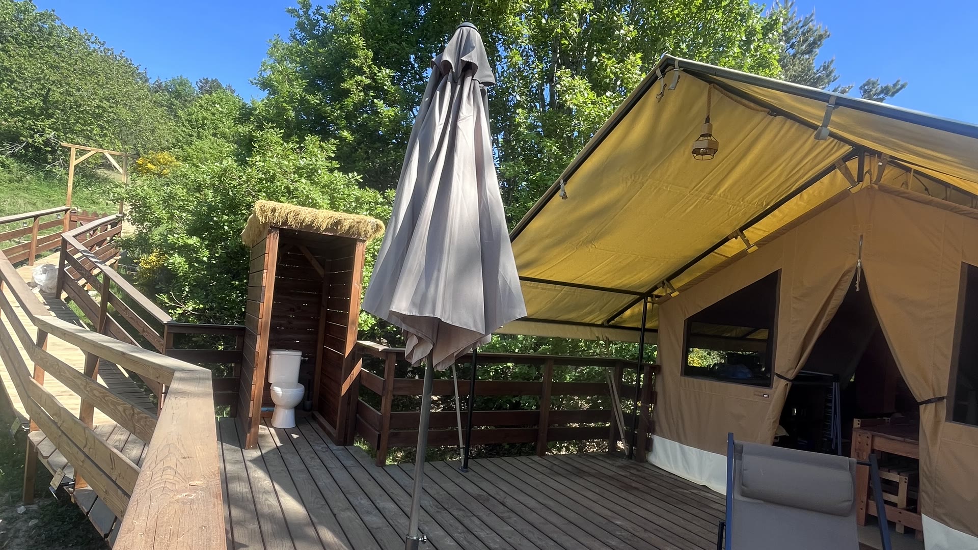 Terrasse en bois de la tente safari du Domaine Solio, parasol ouvert et cabanon des WC, face à la vallée
