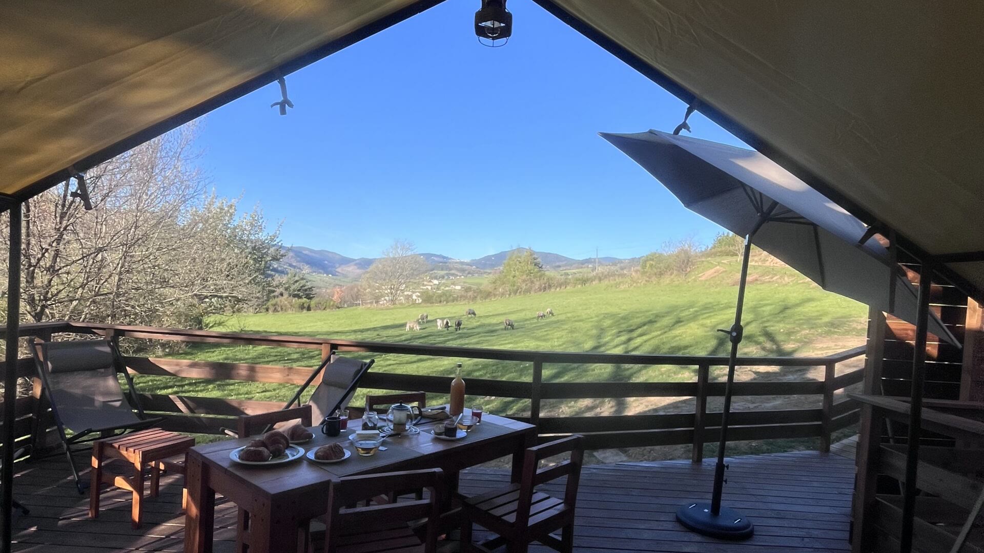 Terrasse en bois de l’Aventura Lodge, table dressée sous la tente safari, ouverte sur la vallée verdoyante