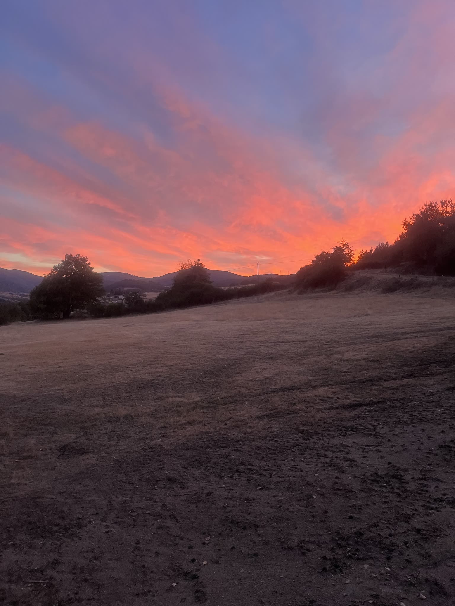 Coucher de soleil rose et orangé au-dessus du pré du Domaine Solio, collines d'Ardèche à l'horizon