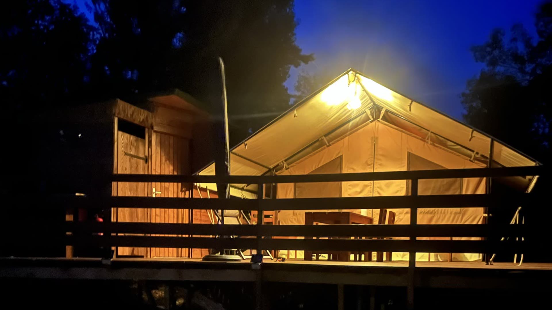 La tente safari L'Estiva éclairée de l'intérieur à la nuit tombée, sous un ciel bleu nuit, au Domaine Solio en Ardèche