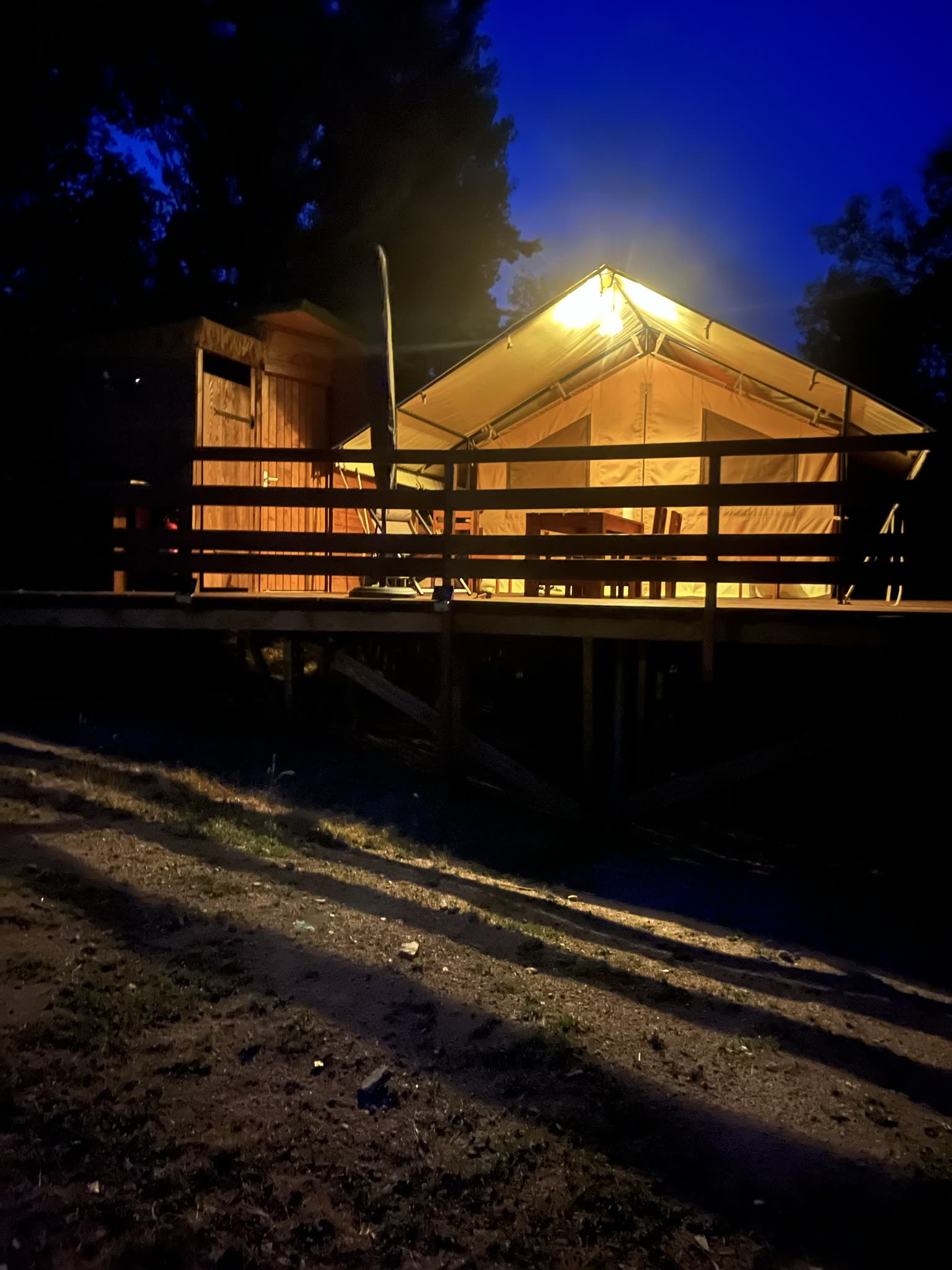 La tente safari L'Estiva éclairée de l'intérieur à la nuit tombée, sous un ciel bleu nuit, au Domaine Solio en Ardèche