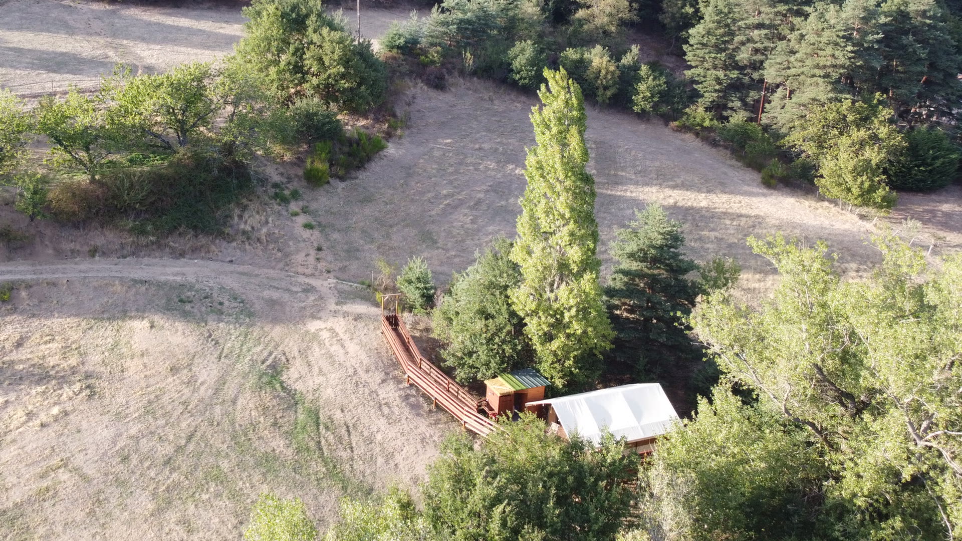 Vue aérienne panoramique du pré du Domaine Solio, la tente safari et sa terrasse à l'extrémité, cernées de forêt