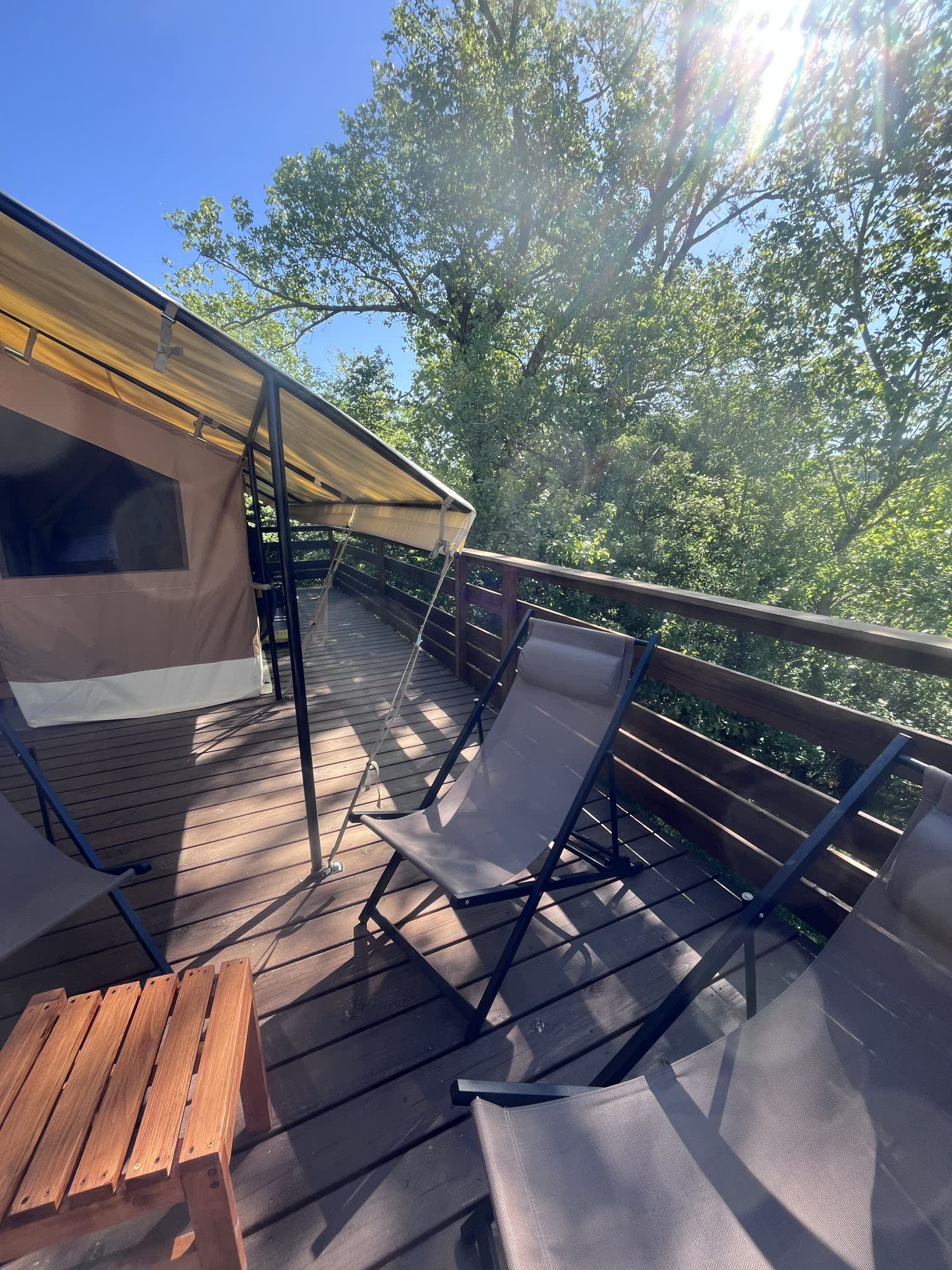 Transats sur la terrasse en bois de la tente safari L'Estiva, à l'ombre de l'auvent, face aux arbres du Domaine Solio