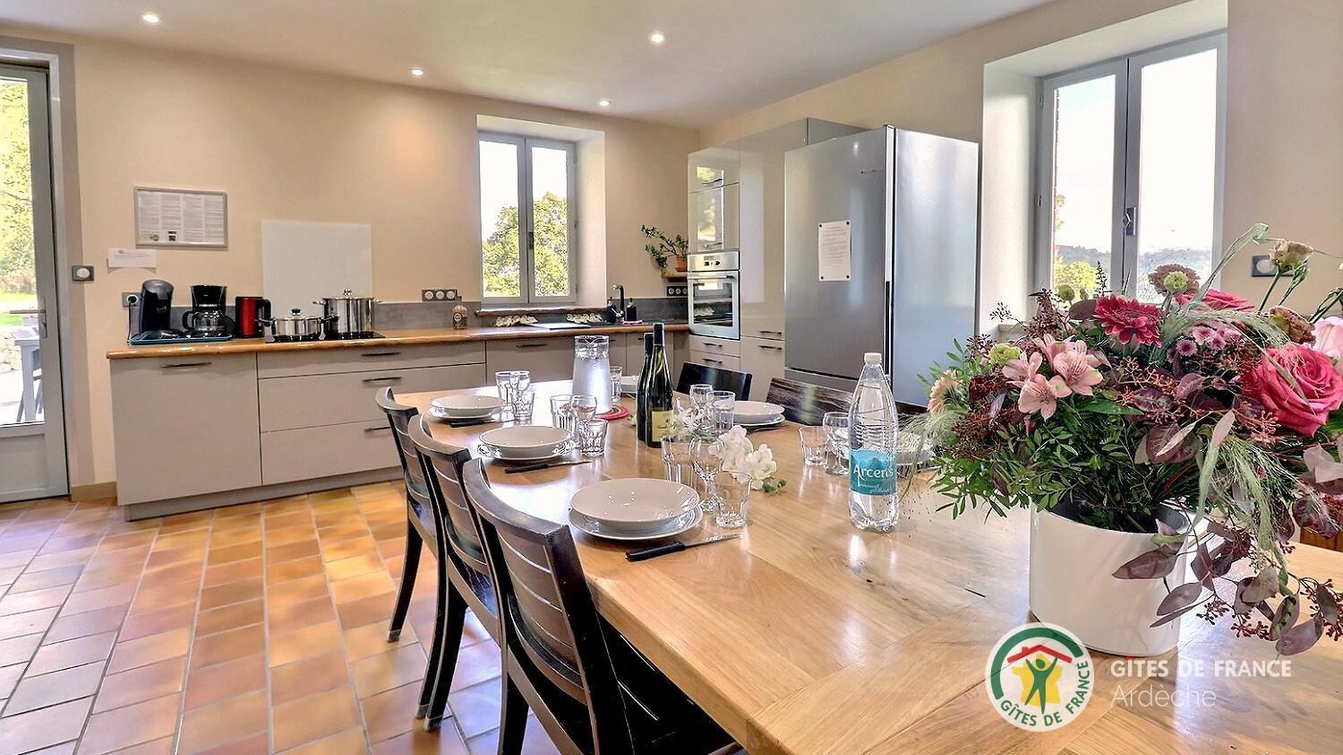 Cuisine équipée du gîte ouverte sur la table dressée, avec un bouquet de fleurs