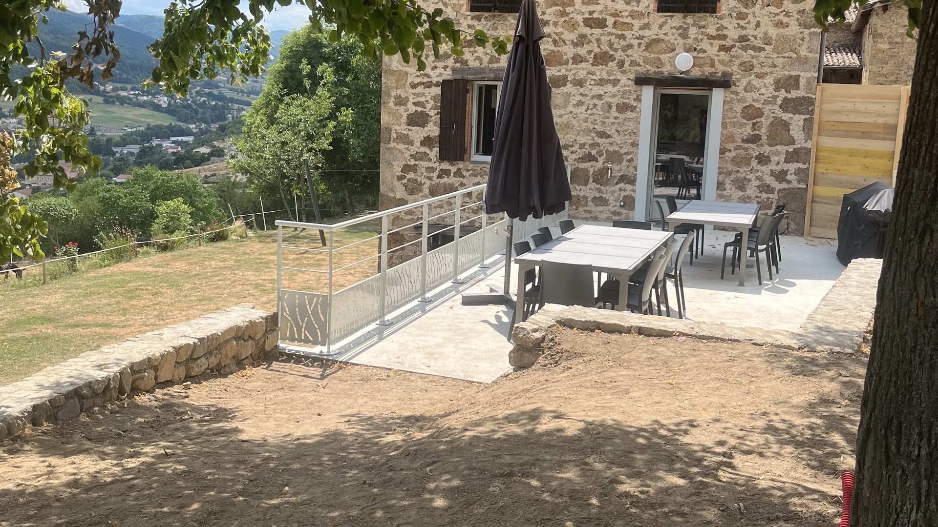 Façade en pierre du gîte La Granja et sa terrasse meublée, face à la vallée ardéchoise