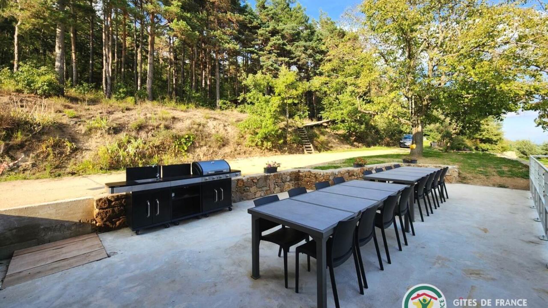 Longue tablée dressée en extérieur devant le gîte, avec le barbecue, face à la prairie et à la forêt