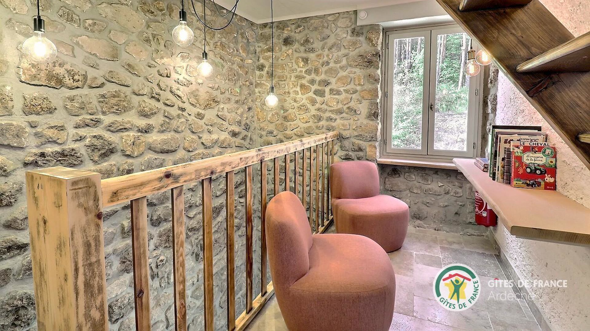 Mezzanine du gîte avec fauteuils, bibliothèque et mur de pierre apparente