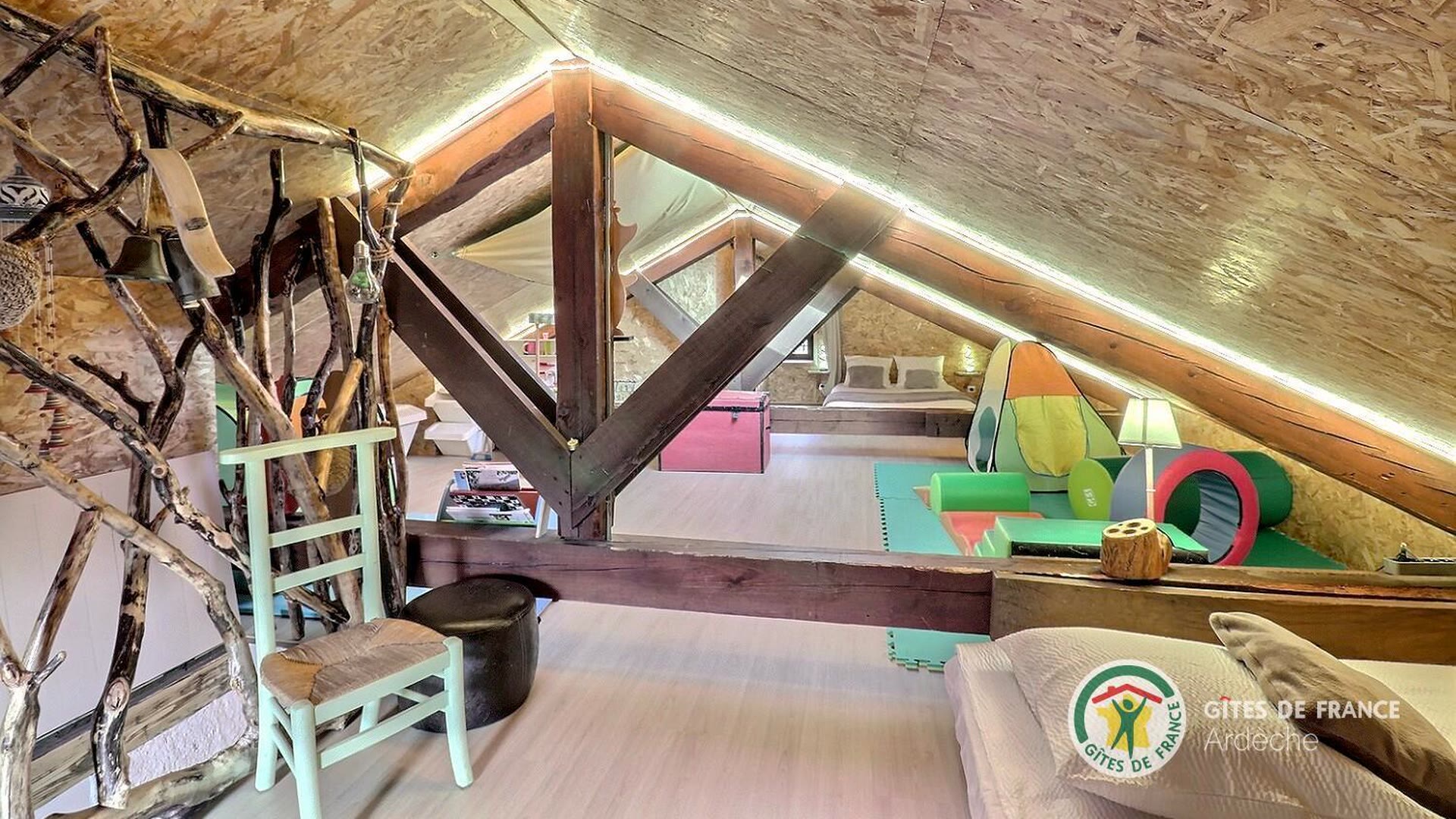 Salle de jeux aménagée dans les combles du gîte, charpente apparente et jouets pour enfants
