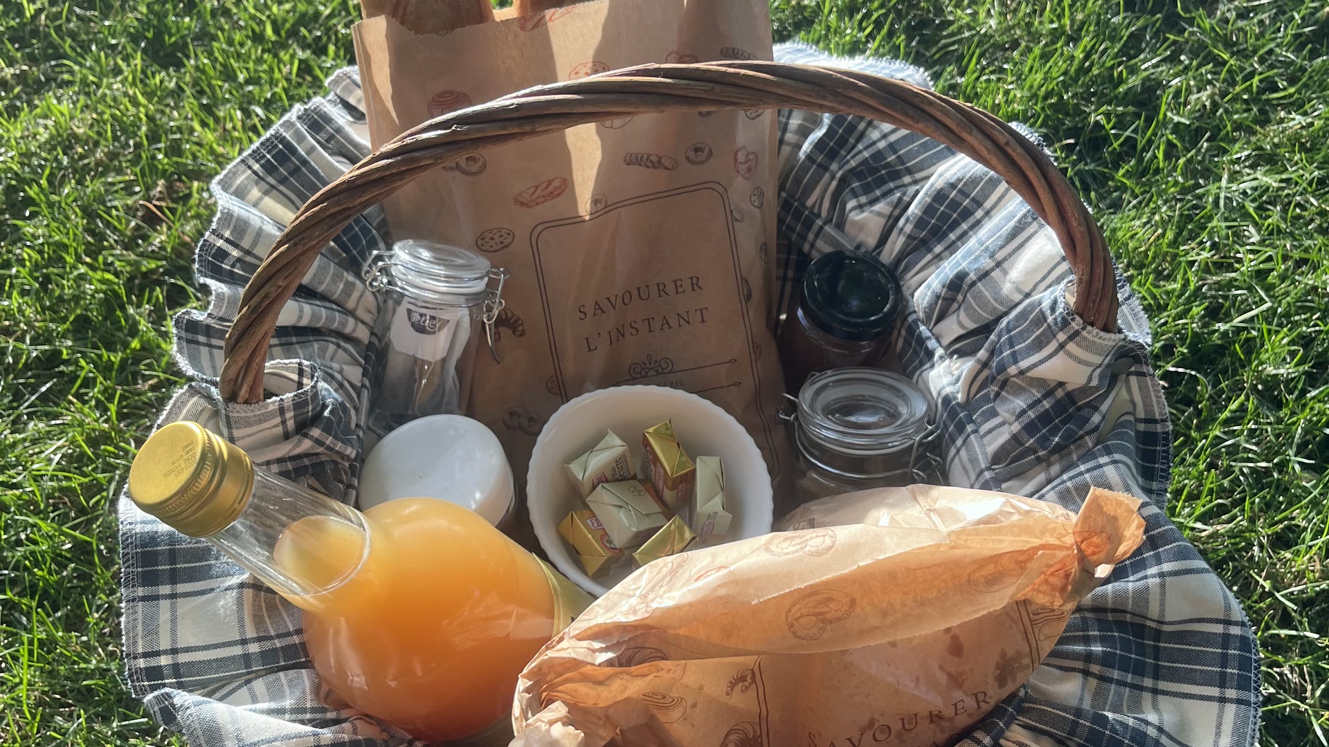 Panier en osier garni de pain, jus d'orange, confitures et beurre, posé dans l'herbe du Domaine Solio