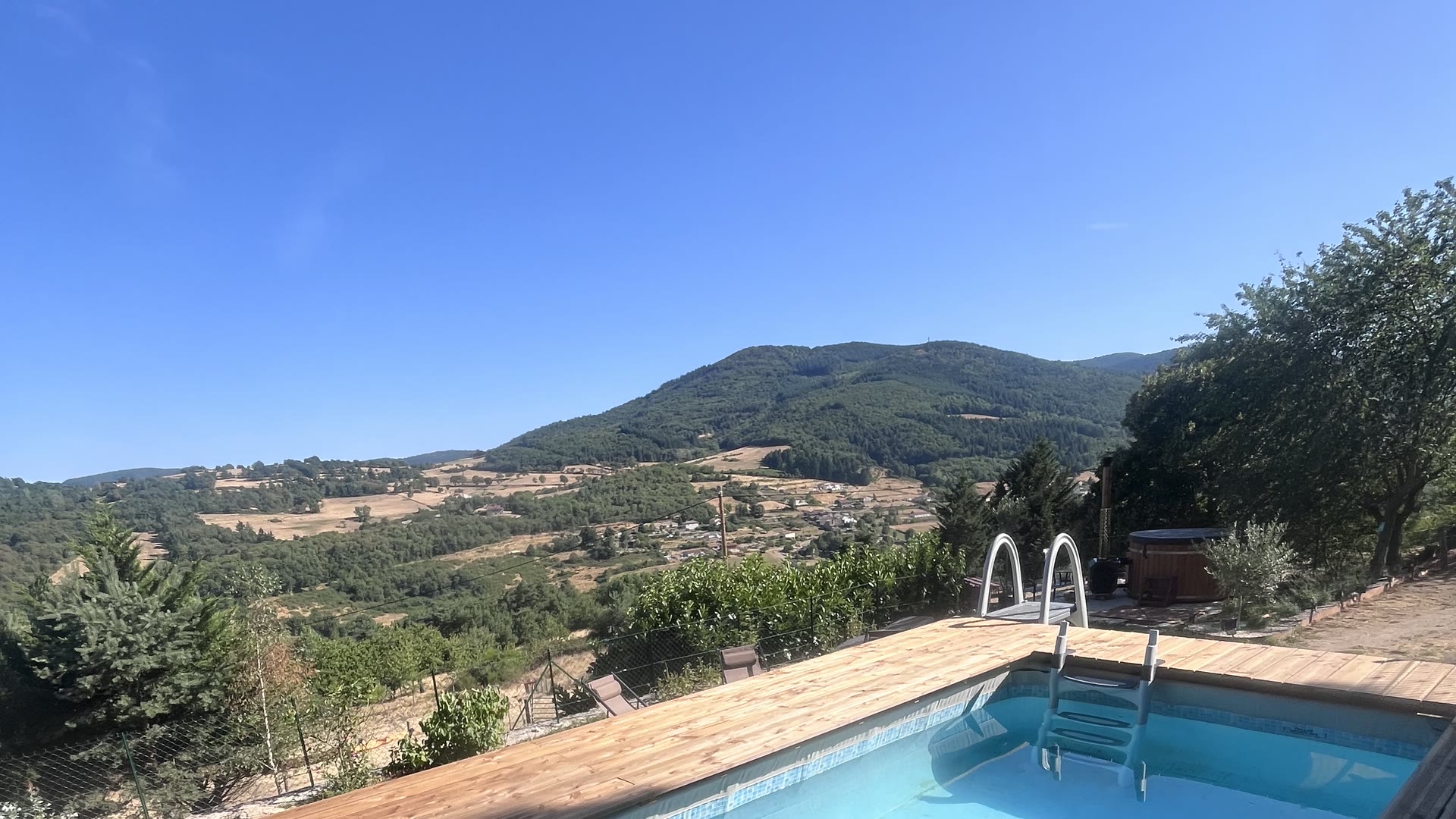 Piscine du Domaine Solio et sa plage en bois, ouverte sur la vallée et les collines boisées