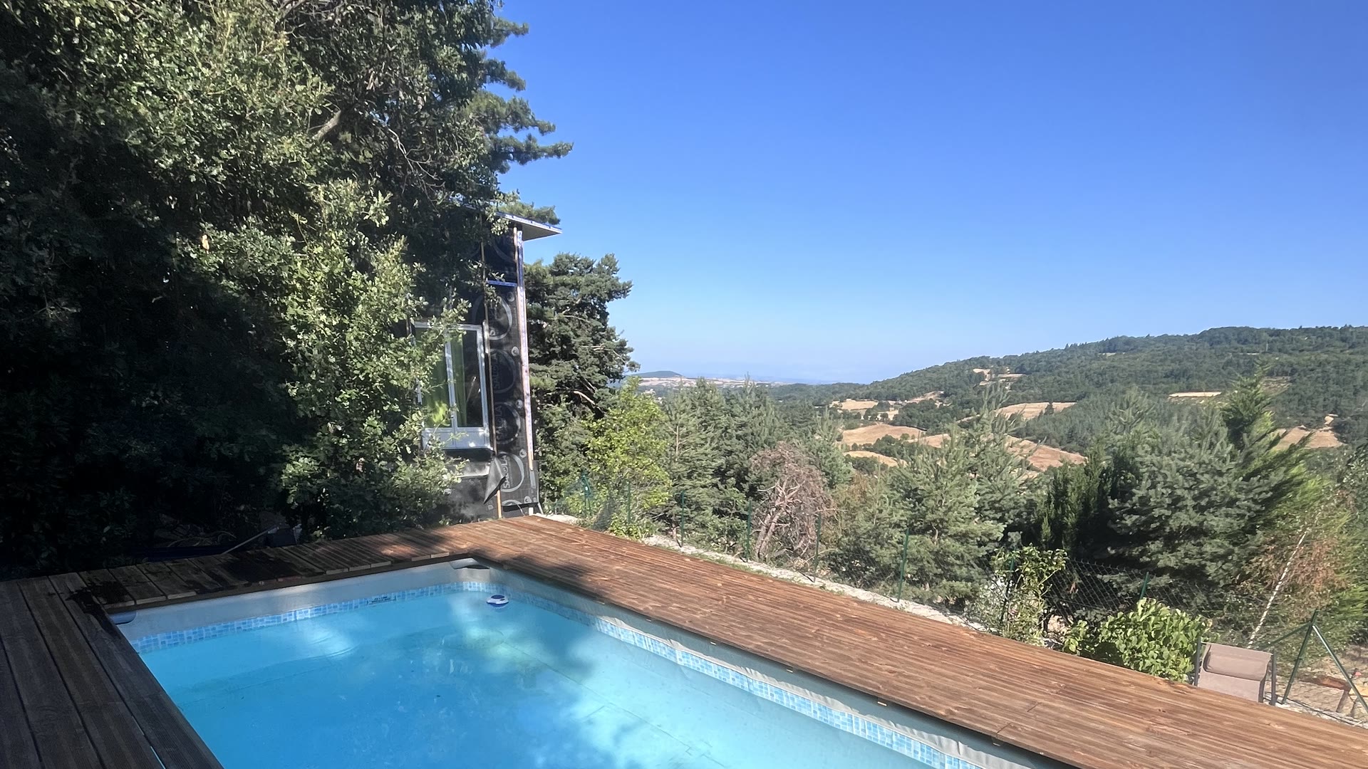 Piscine bordée d'une plage en bois au Domaine Solio, les collines de l'Ardèche à l'horizon
